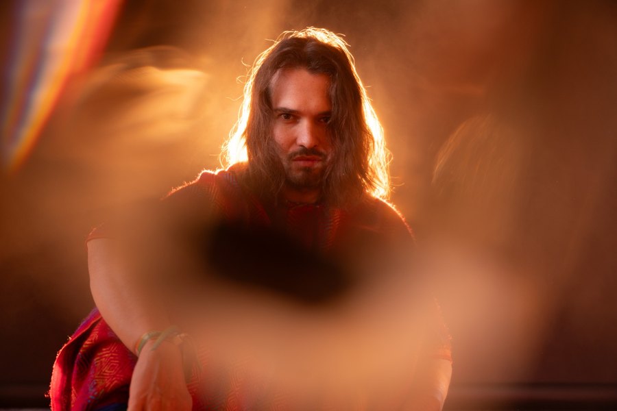 Man with long hair in a woven red poncho, backlit through warm haze