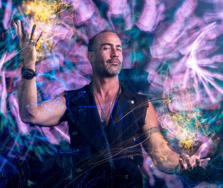 Man in a black vest surrounded by swirling purple and gold light trails