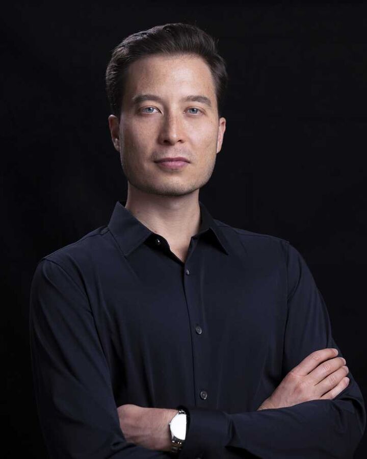 Man in a dark shirt with arms crossed against a black background