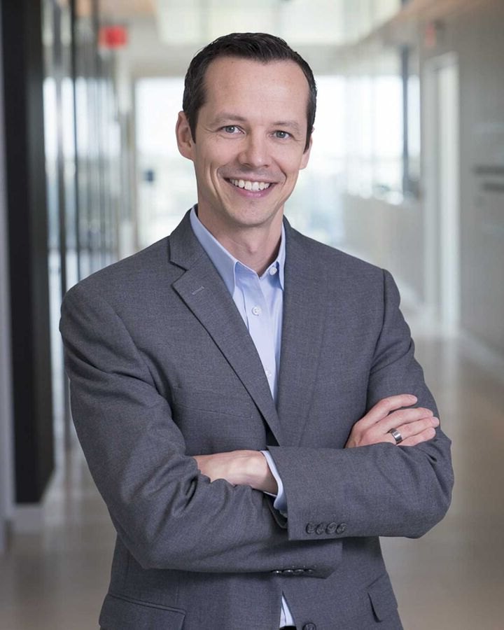 Man in a grey suit with arms crossed in a modern office