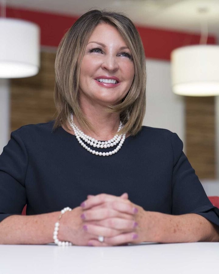 Smiling woman in a navy dress and pearls seated at a table