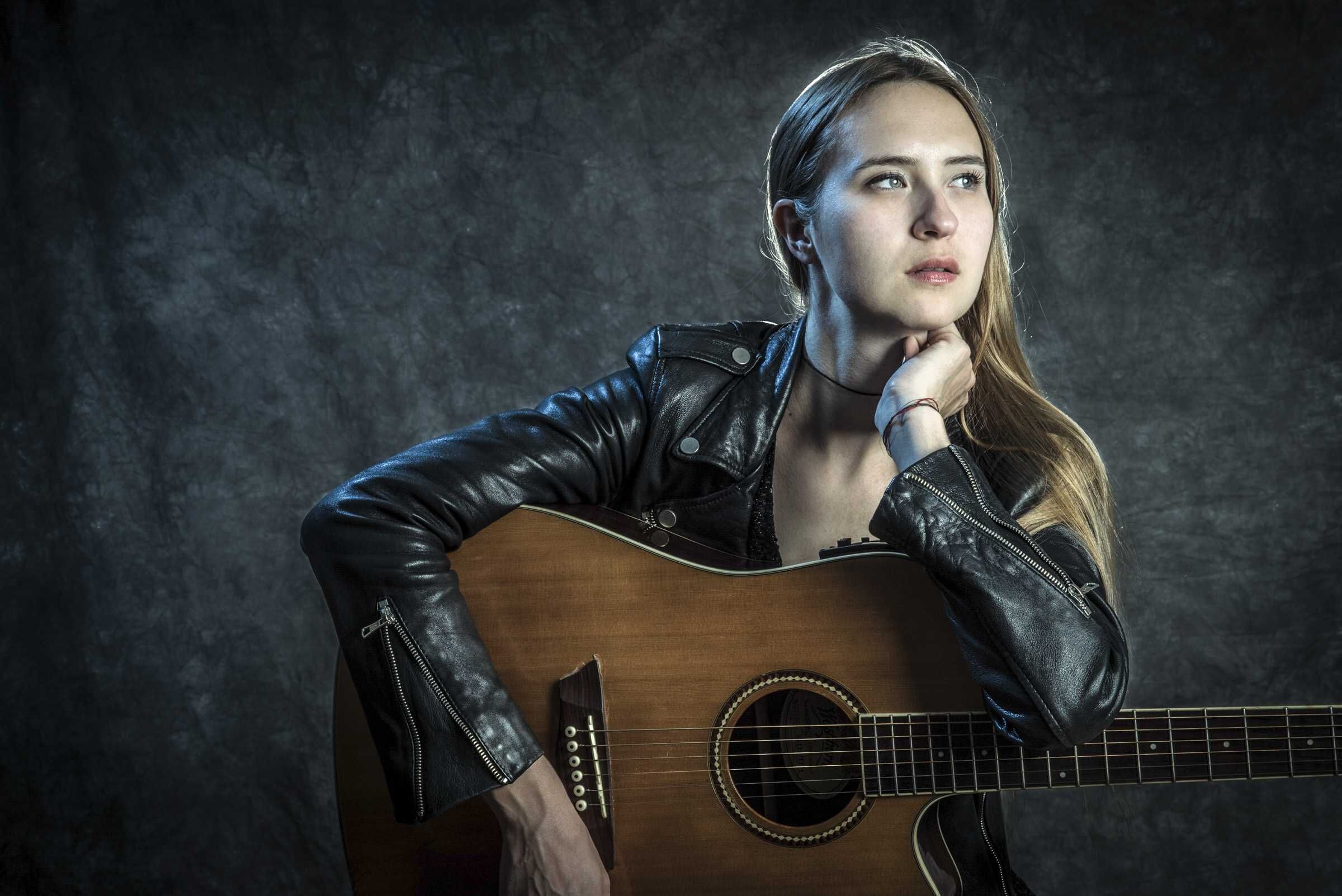 Musician in a leather jacket resting on an acoustic guitar