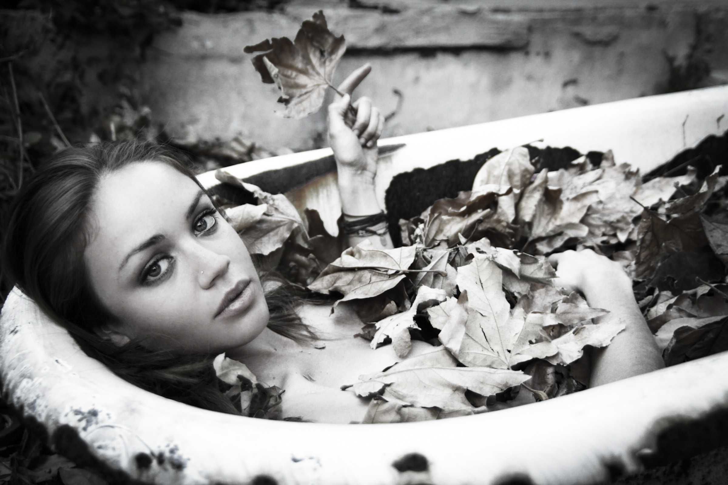 Black and white portrait of a woman lying among leaves in a bathtub