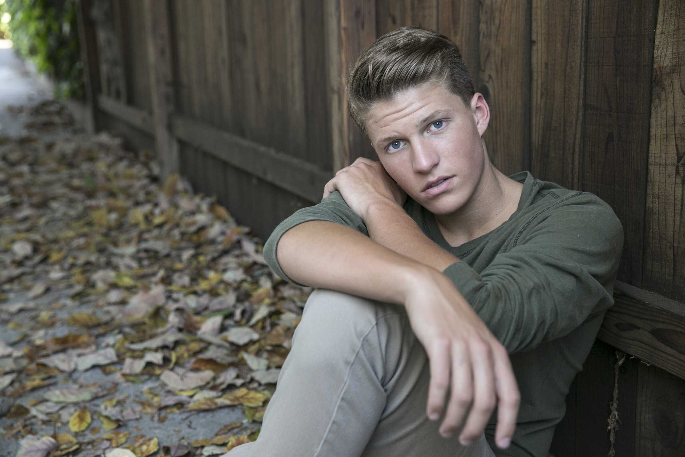 Young man sitting by a fence among autumn leaves