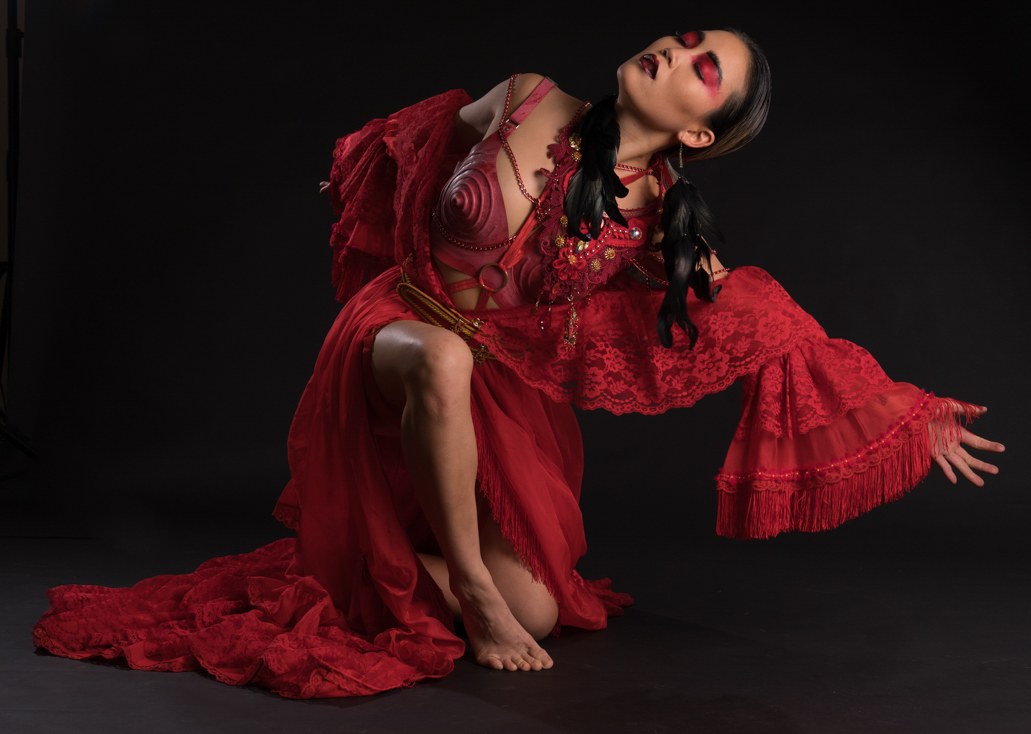 Dancer in a flowing red lace gown and feathers, kneeling with head thrown back