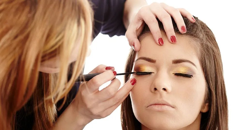Makeup artist applying eyeliner to a woman with gold eyeshadow